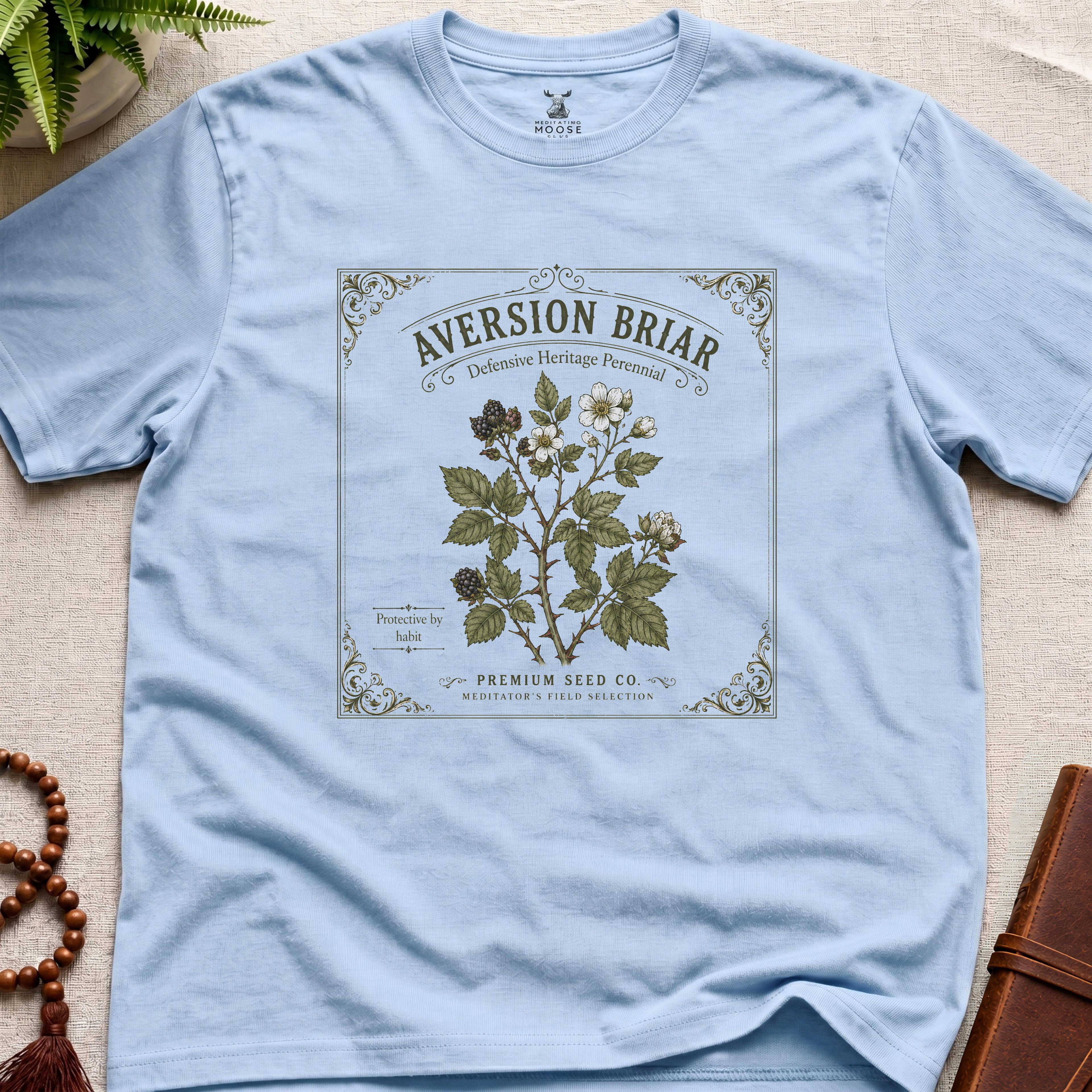 Light blue t-shirt with a botanical label design on a beige surface.