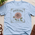 Light blue t-shirt with a vintage seed packet style flower graphic doubting dahlia showstopping bloom