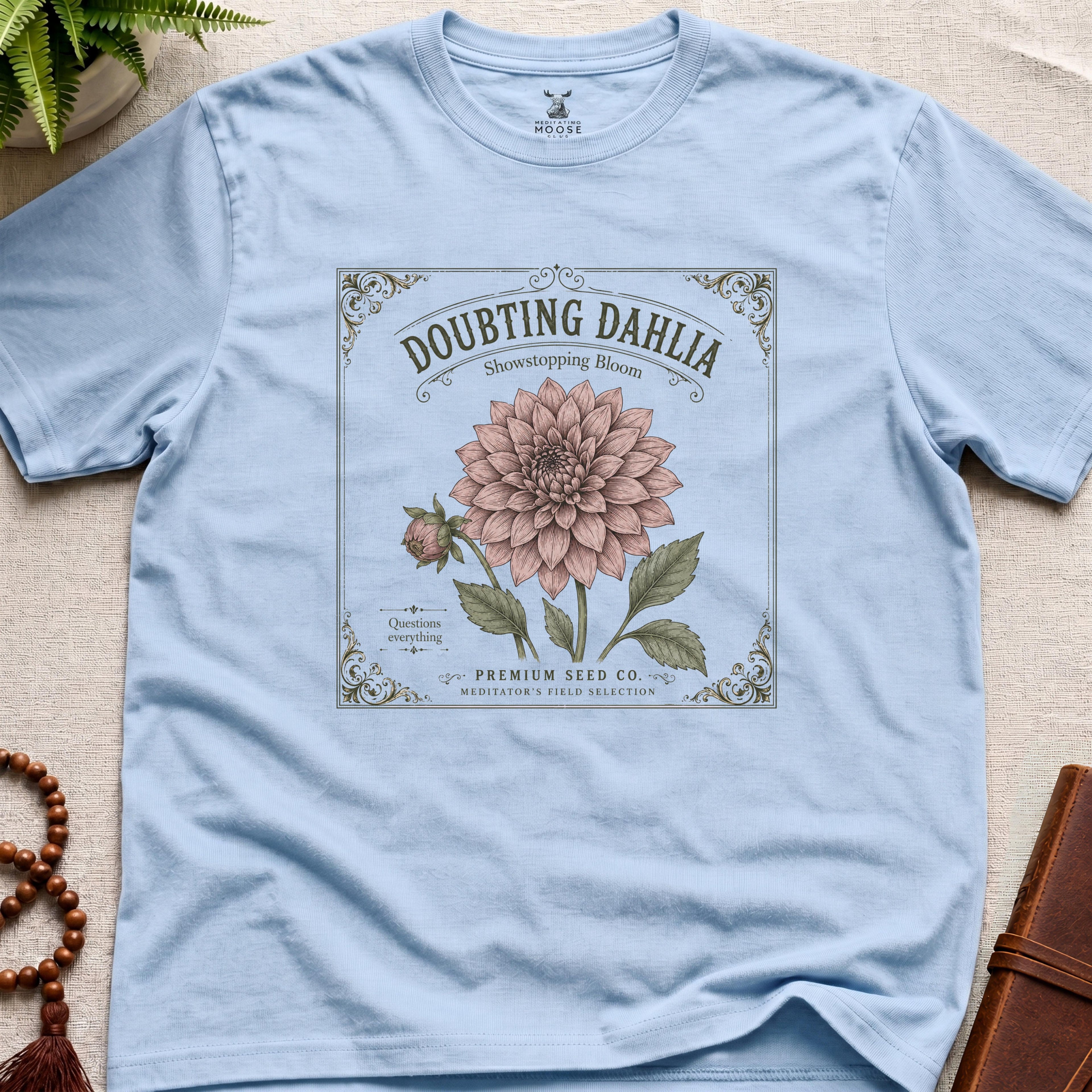 Light blue t-shirt with a vintage seed packet style flower graphic doubting dahlia showstopping bloom
