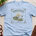 Light blue t-shirt with vintage-style seed packet water lily graphic on a beige surface