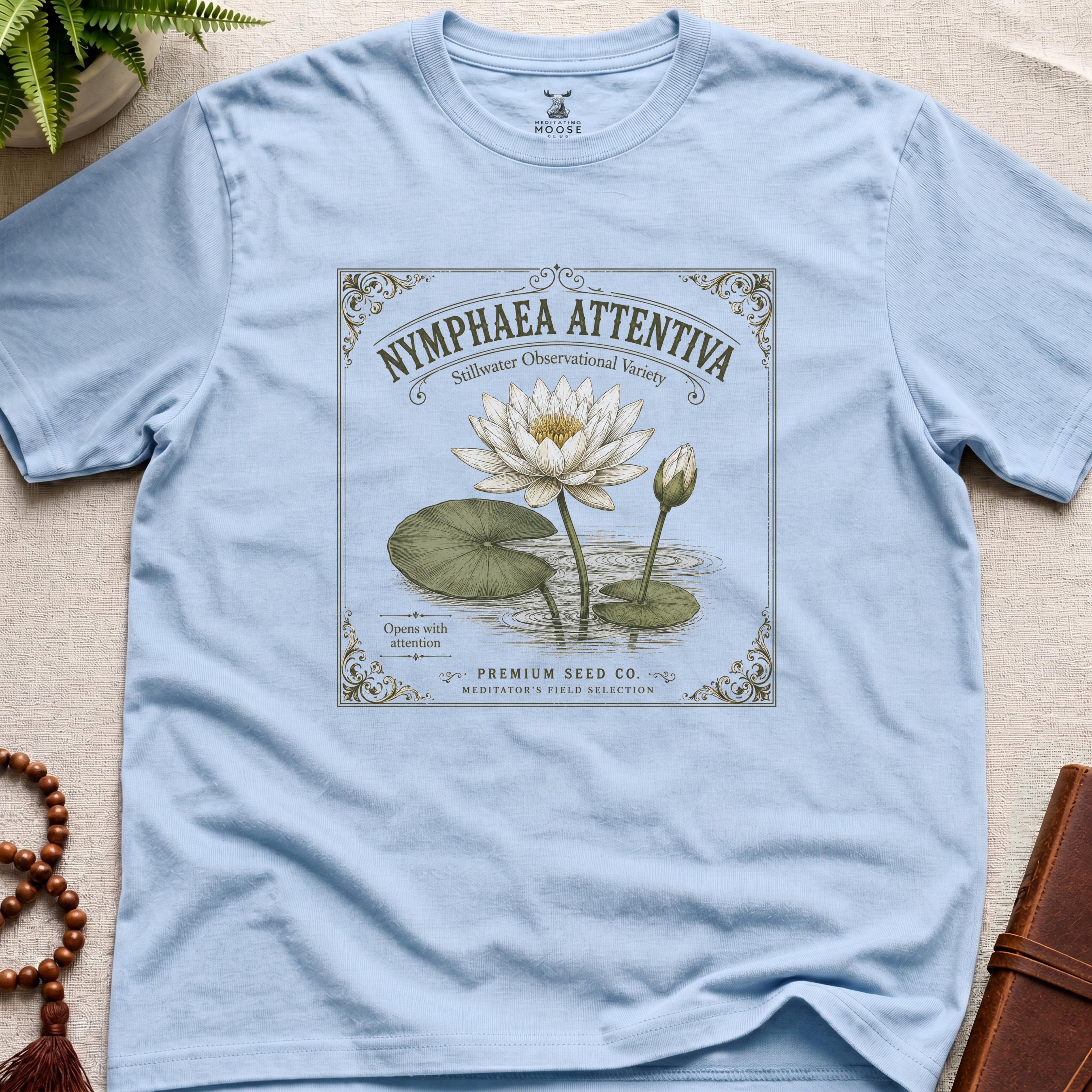 Light blue t-shirt with vintage-style seed packet water lily graphic on a beige surface