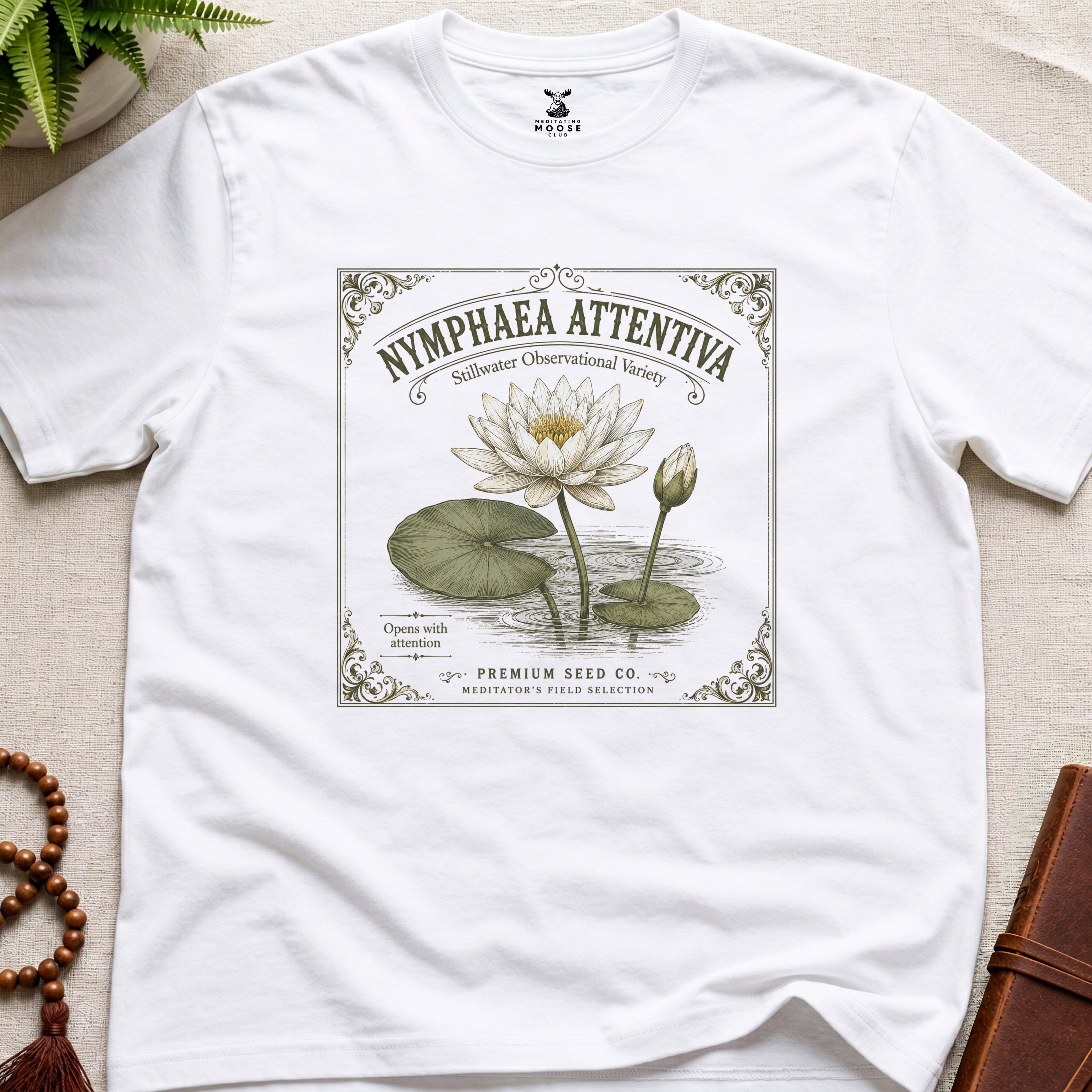 White t-shirt with vintage-style seed packet water lily graphic on a beige surface