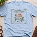 Light blue t-shirt with vintage see packet style, returning rose design on a beige surface.