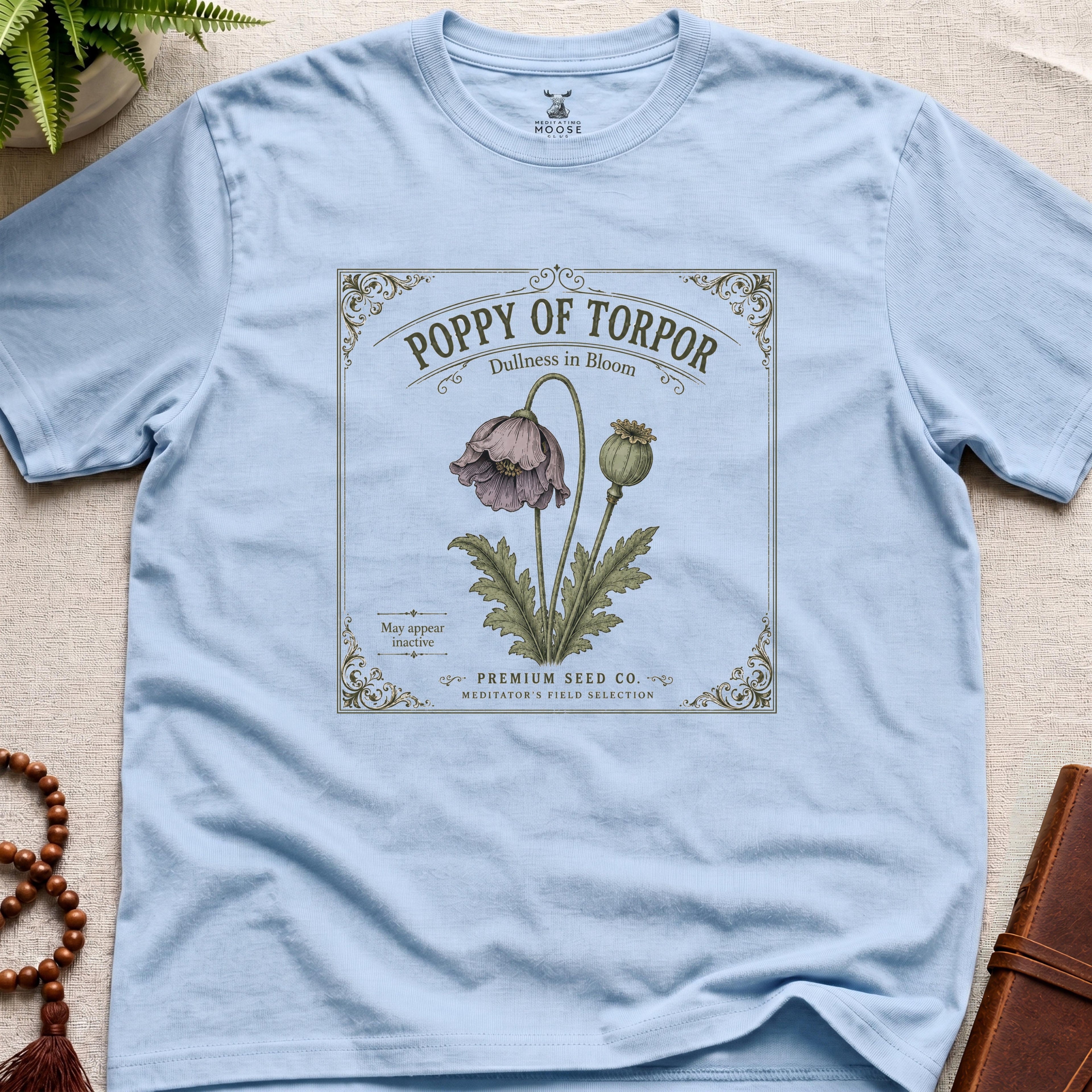 Light blue t-shirt with a vintage-style poppy seed packet design on a beige surface.