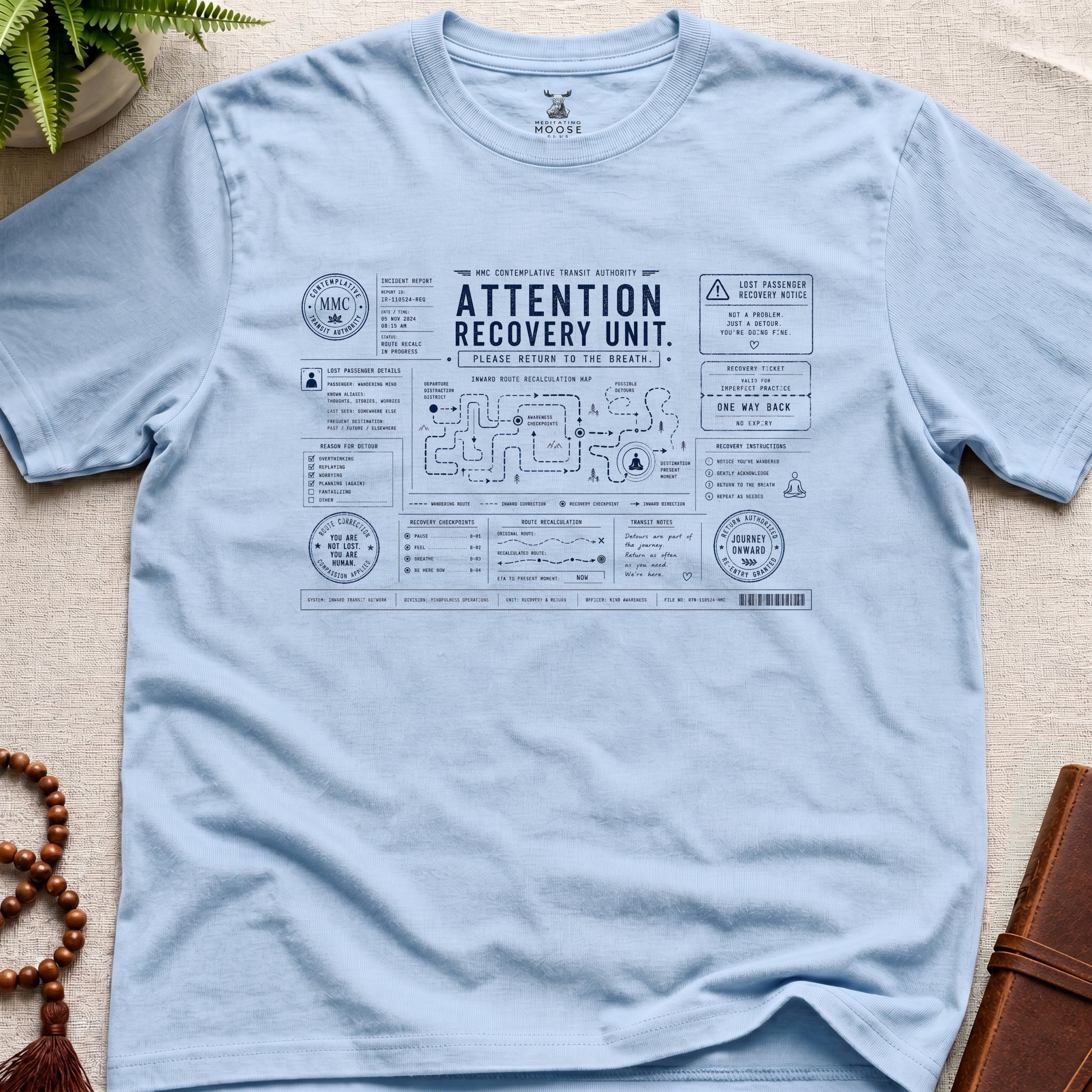 Light blue mindfulness transit recovery t-shirt graphic reading “Attention Recovery Unit” with inward rerouting diagrams and contemplative navigation systems.