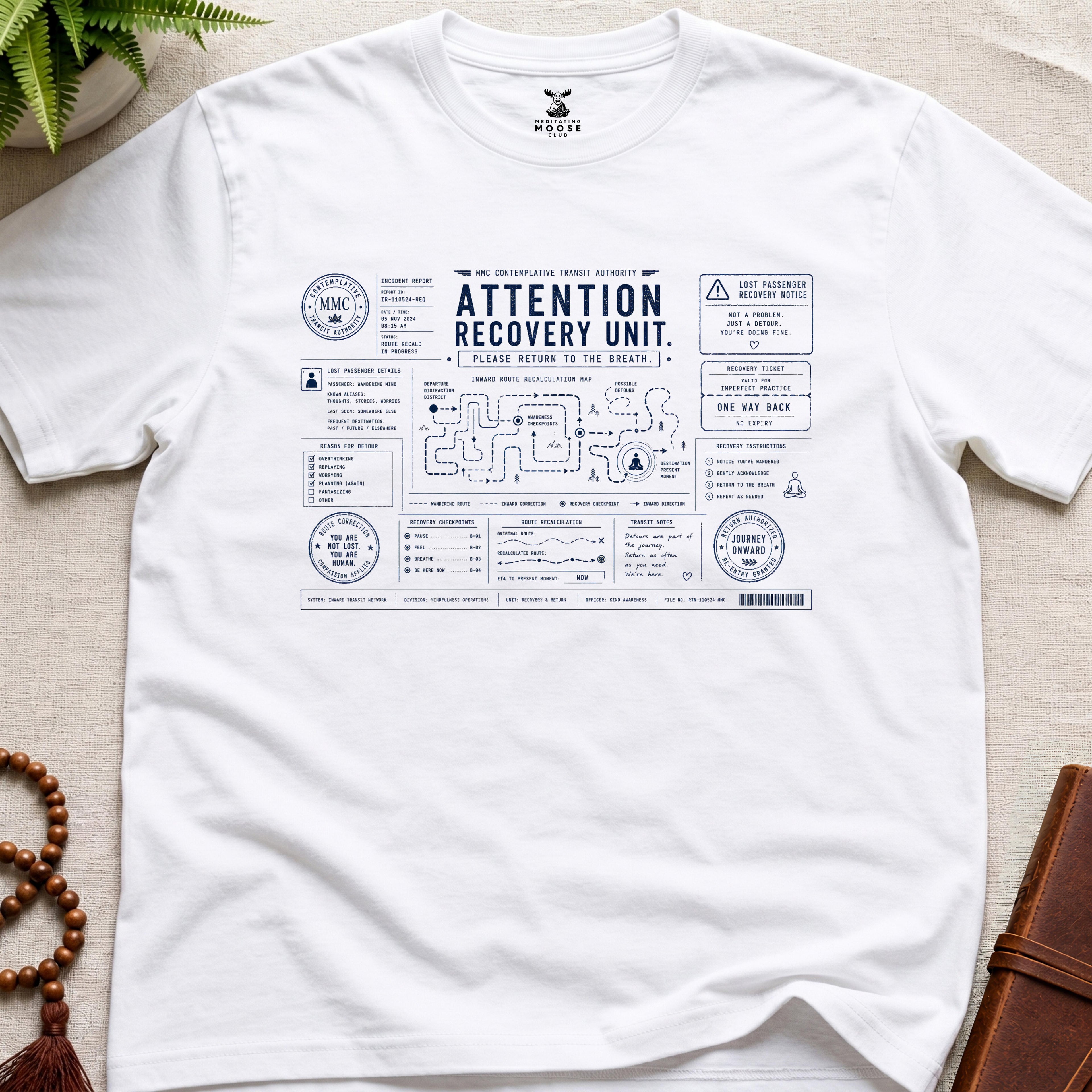 White mindfulness transit recovery t-shirt graphic reading “Attention Recovery Unit” with inward rerouting diagrams and contemplative navigation systems.
