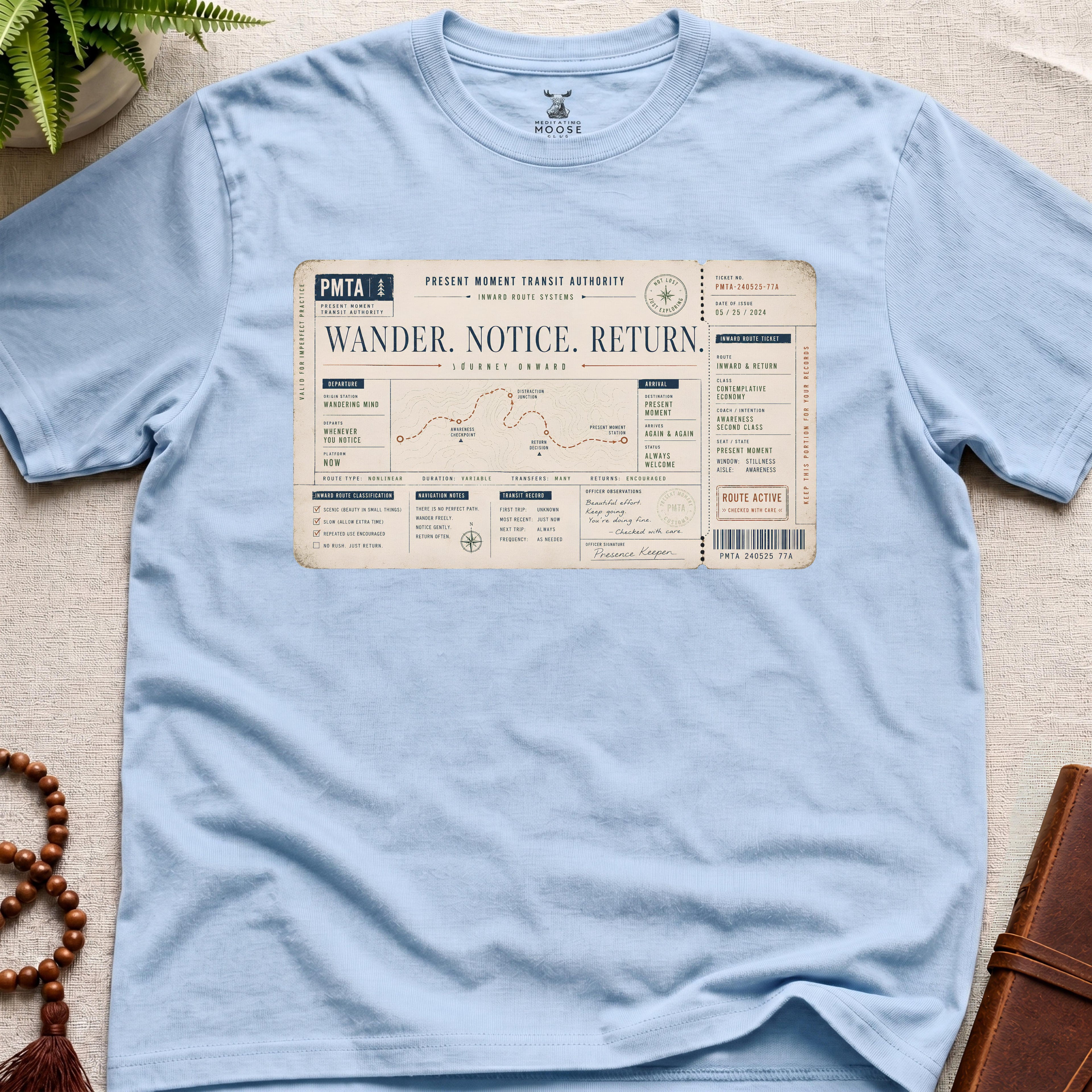 Light blue vintage-style inward transit ticket t-shirt graphic featuring the phrase “Wander. Notice. Return.” with contemplative route systems and awareness checkpoints.