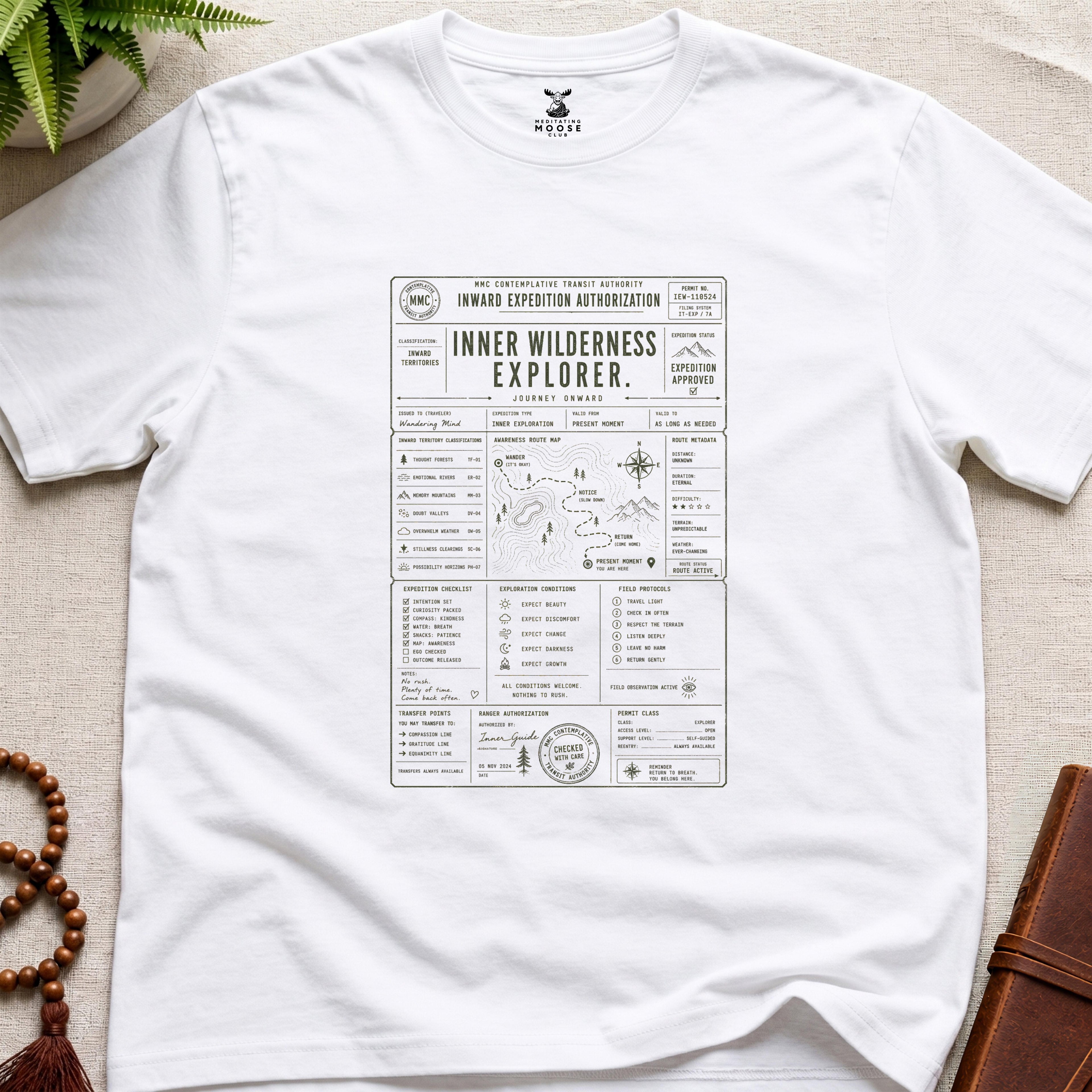 White contemplative inward expedition permit t-shirt graphic reading “Inner Wilderness Explorer” with navigation charts and mindfulness field systems.