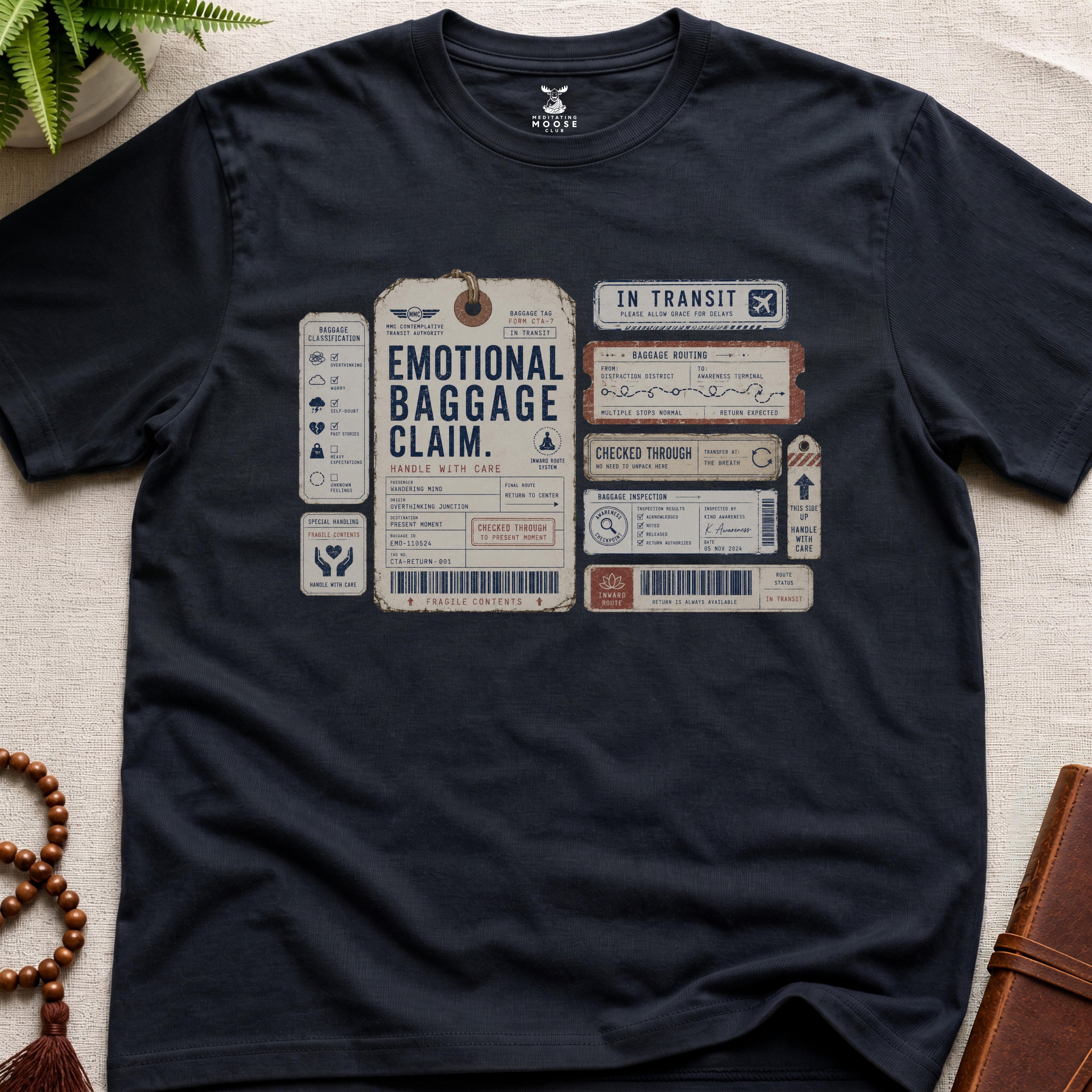 Black vintage baggage-tag inspired mindfulness t-shirt graphic reading “Emotional Baggage Claim” with contemplative transit handling marks.