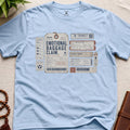 Light blue vintage baggage-tag inspired mindfulness t-shirt graphic reading “Emotional Baggage Claim” with contemplative transit handling marks.