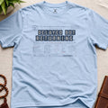 Light blue vintage arrival-board inspired meditation t-shirt reading “Delayed But Returning” with contemplative transit typography.