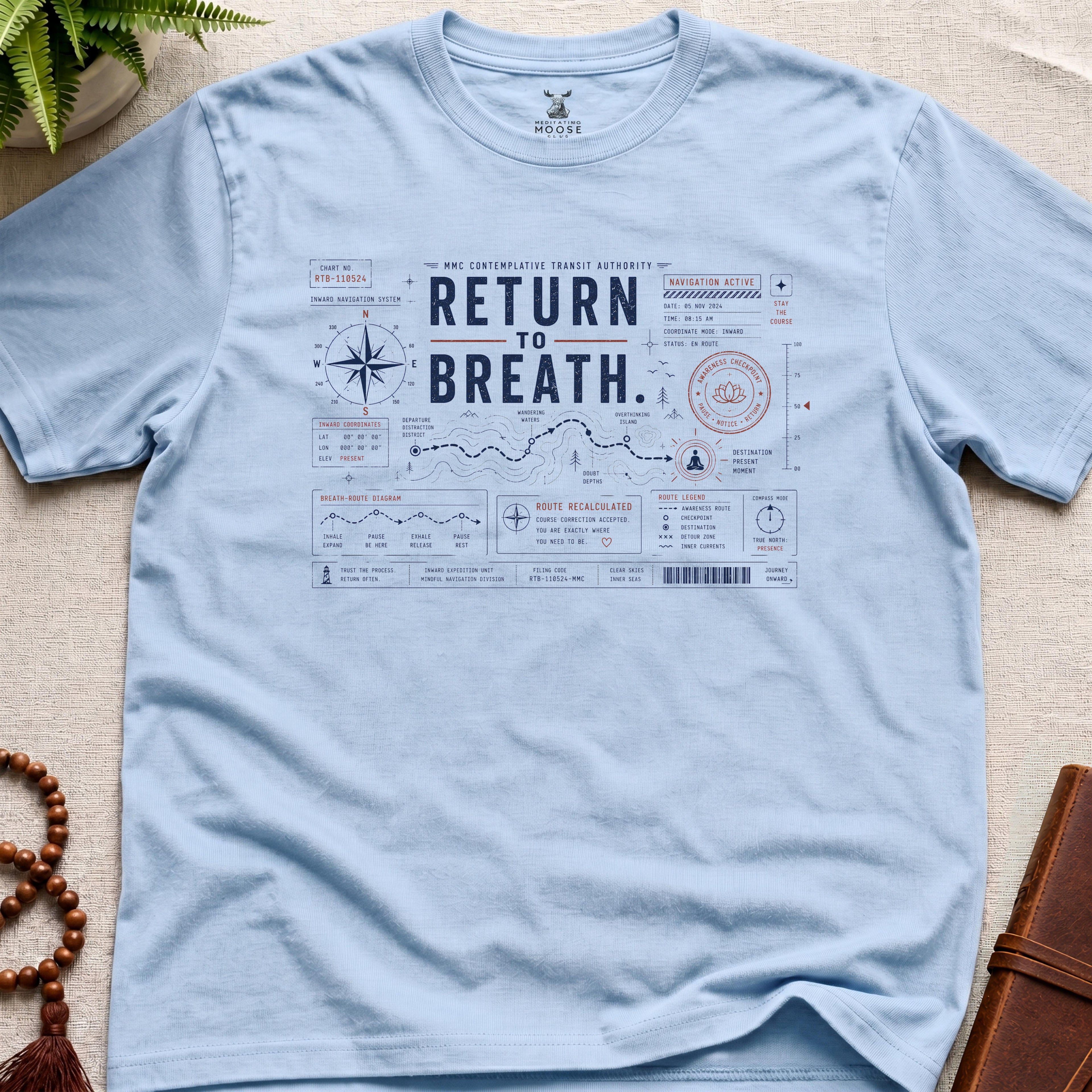Light blue contemplative navigation-chart t-shirt graphic reading “Return To Breath” with compass systems and inward route diagrams.