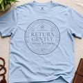 Light blue contemplative circular re-entry approval stamp t-shirt graphic reading “Return Gently” with passport-style typography and mindfulness transit authority markings.