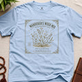 Light blue t-shirt with 'Wanderer's Weed Mix' seed packet design on a beige surface.