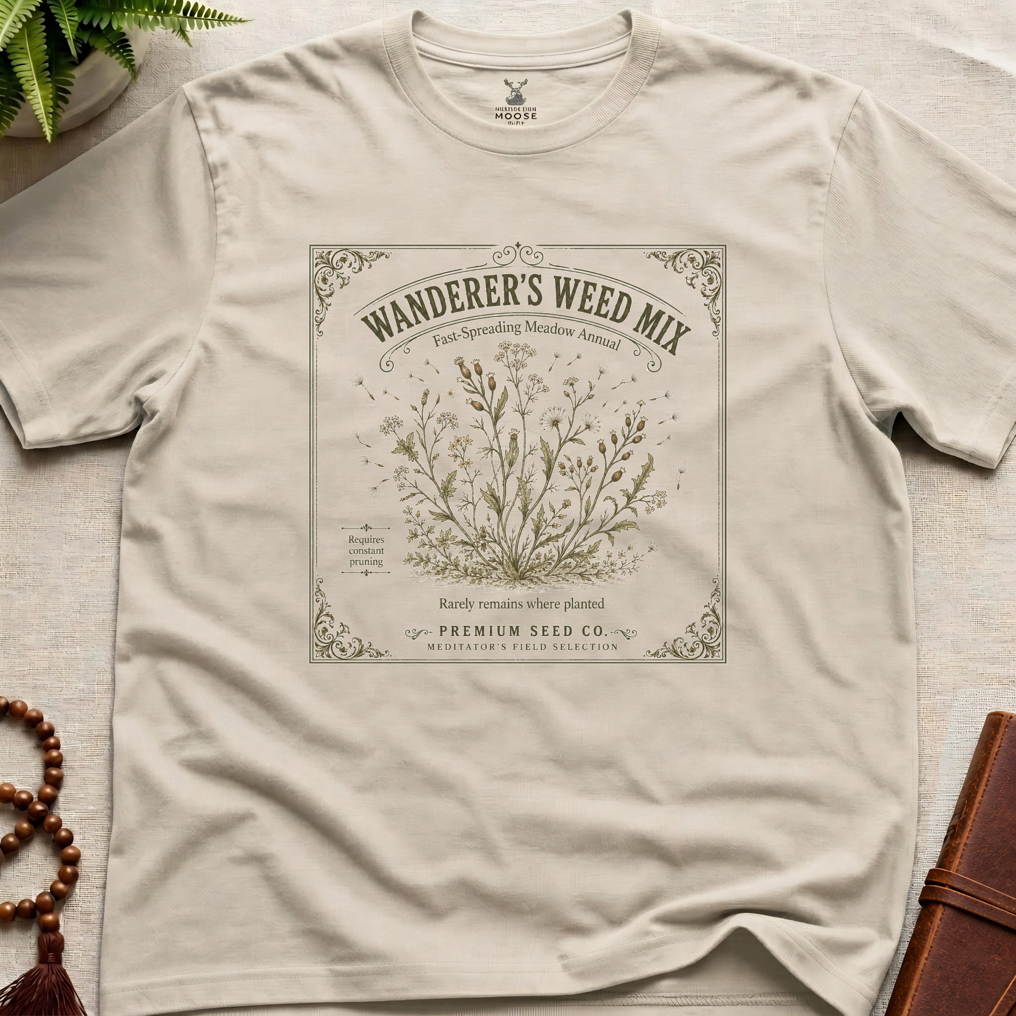Beige t-shirt with 'Wanderer's Weed Mix' seed packet design on a light surface.