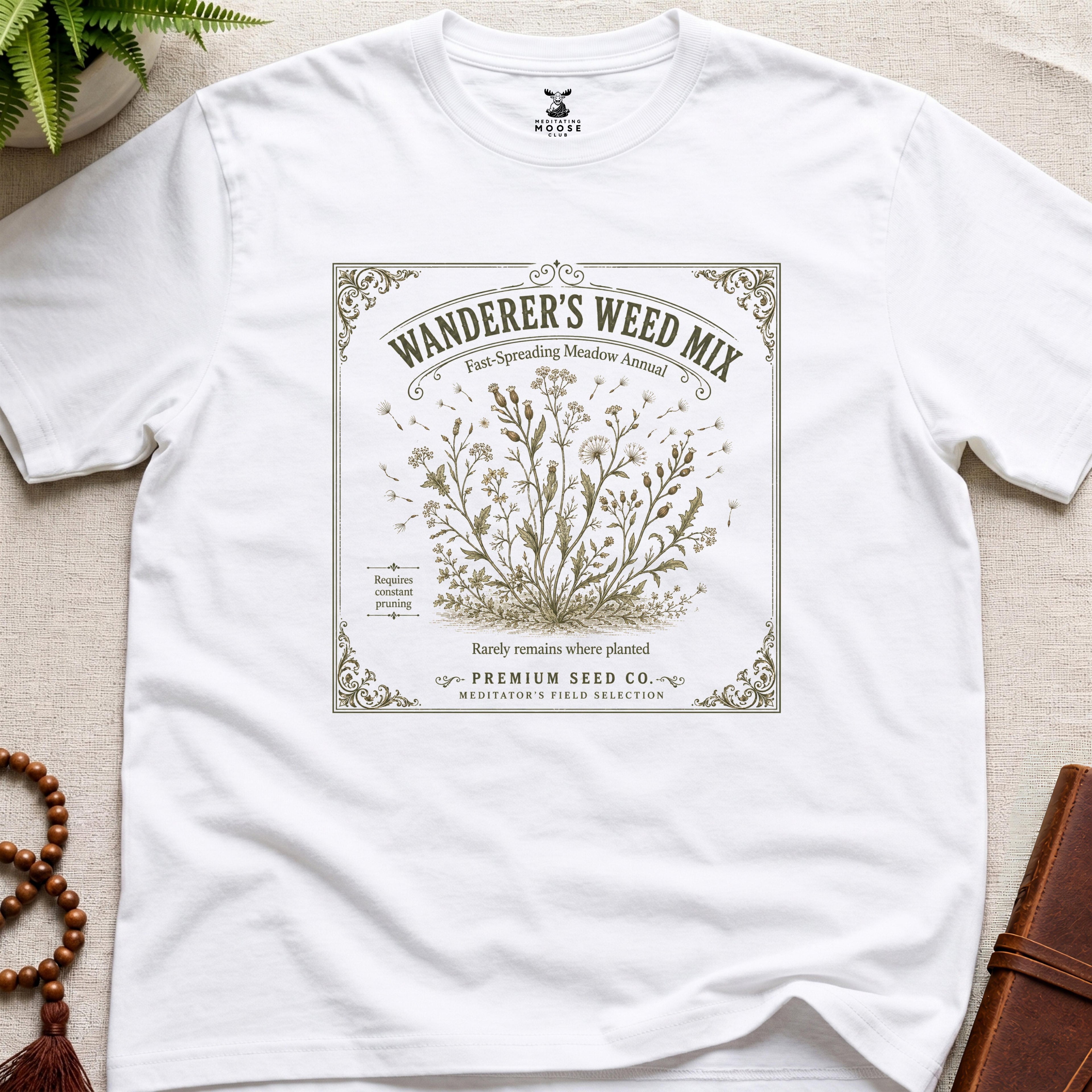 White t-shirt with 'Wanderer's Weed Mix' seed packet design on a beige surface.